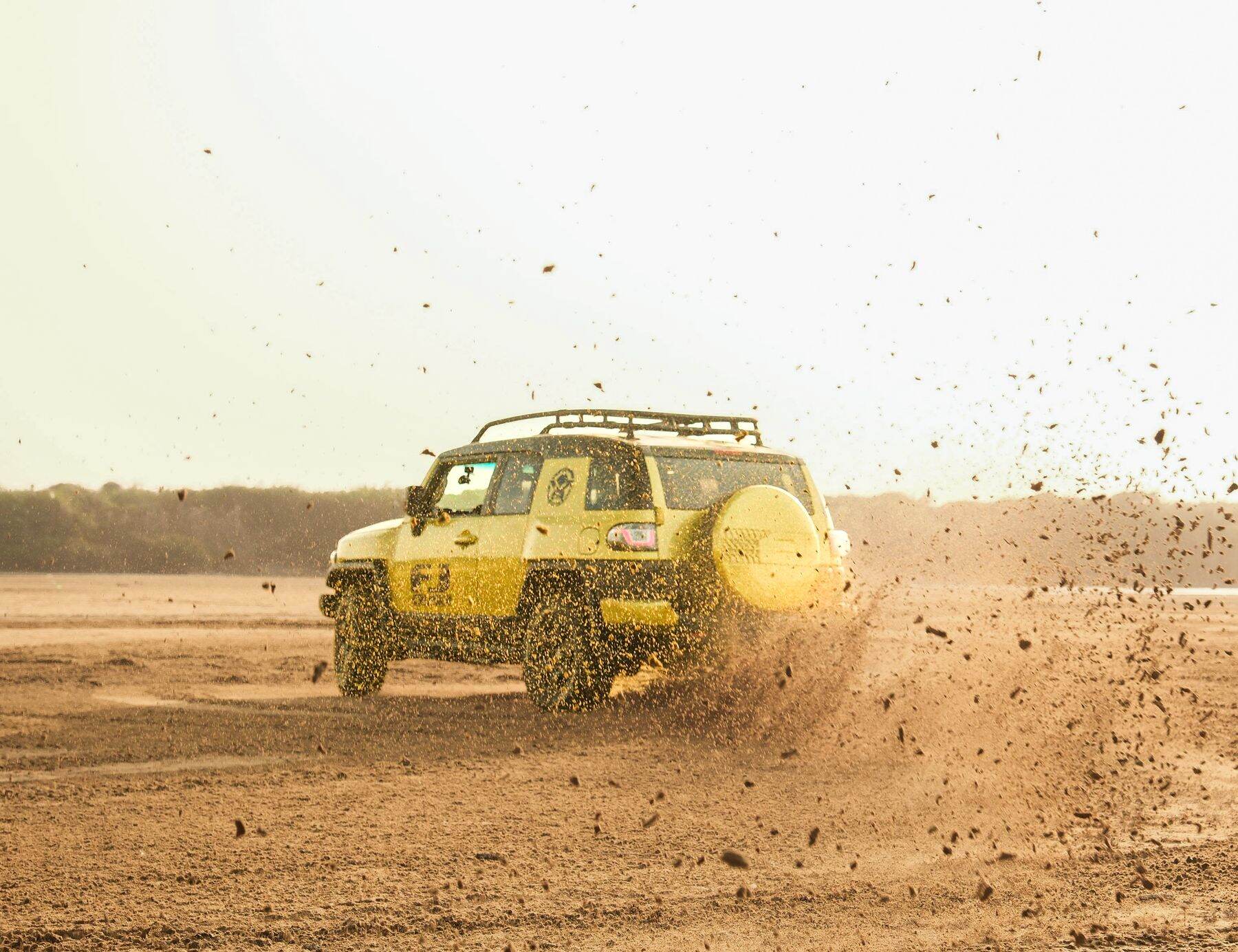 A yellow SUV kicking up dust on a dirt road